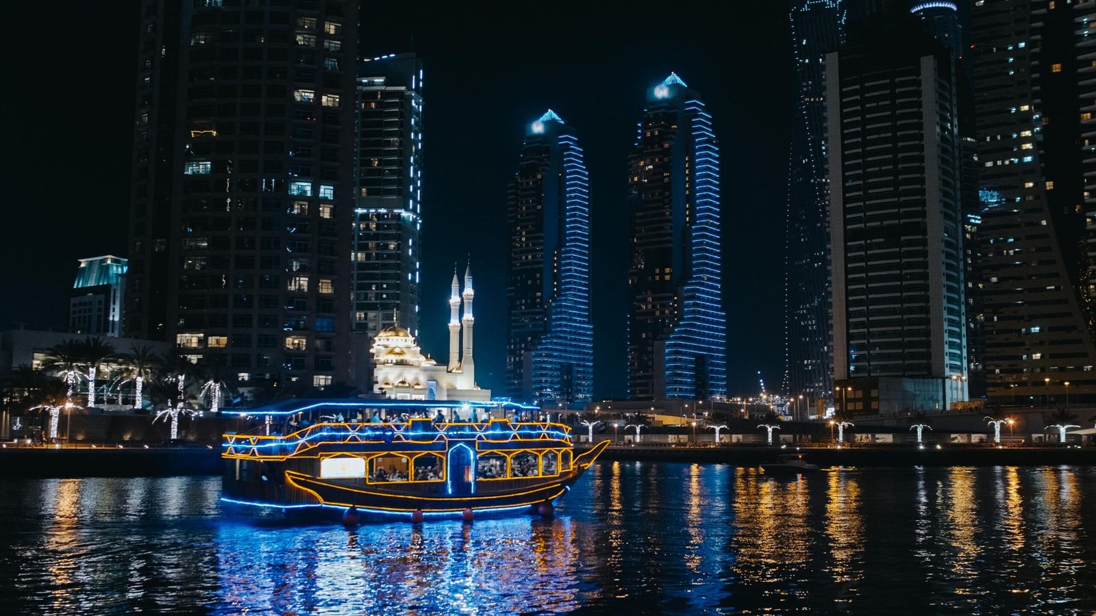 Stunning Dubai marina skyline at night with illuminated buildings and cruise boat on the water.